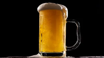 A beer mug with foam stands on a black background.