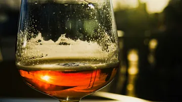 A glass with a drink stands, fogged up, in sunlight.