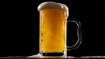 Ein Bierkrug sprudelt über, vor schwarzem Hintergrund.