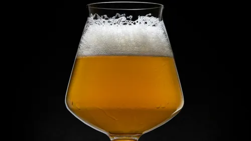 Ein Bierglas mit schaumigem, goldenem Bier vor schwarzem Hintergrund.