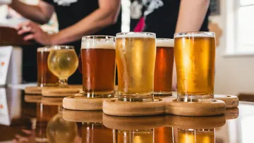 There are six glasses of beer on a wooden board in a bar.