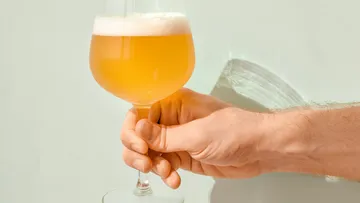 Hand holding a wine glass with a blond drink.