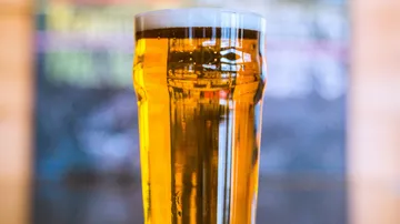 A glass of beer stands in a blurred background.