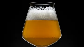 A glass of beer with foam against a black background.