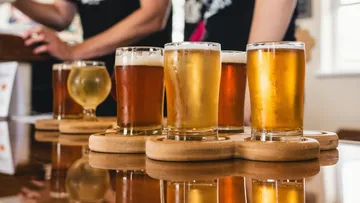 There are six beer glasses on a table with wooden underlays.