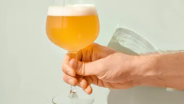 One hand holds a glass of light beer.