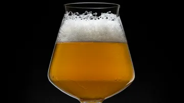 Ein Glas Bier mit Schaum steht vor schwarzem Hintergrund.