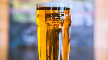 A glass of beer stands in a blurred environment.