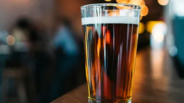 A glass of beer is on a table in a bar.