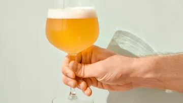 One hand holds a beer glass with a foamy surface.