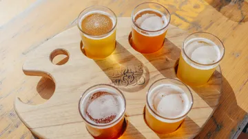 Beer glasses on a wooden board, served together in sunlight.