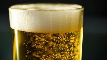 A glass of beer with foam rests on a dark background.