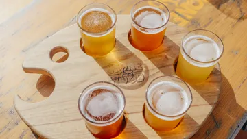 Sechs kleine Biergläser stehen auf einem Holztablett.