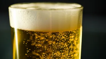 A glass of beer with a frothy surface in a dark background.