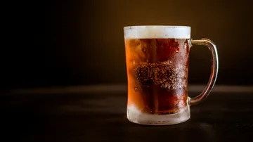 A cold beer glass with ice on a dark table.