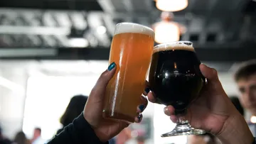 Two glasses toast, surrounded by a crowd of people.