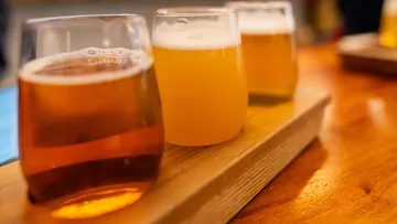 There are three glasses of beer on a wooden board.