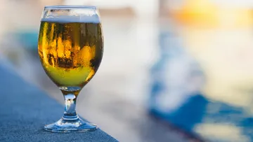 A glass of beer is on a poolside table.