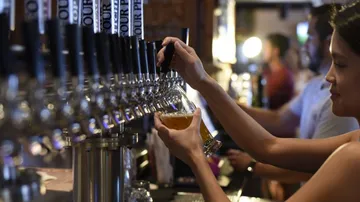 Woman taps beer at a bar with several taps.