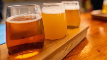 There are three glasses of beer on a wooden board.