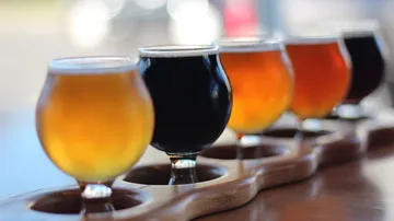 Five glasses of beer sit on a wooden plate.