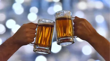 Zwei Bierkrüge stoßen an, verschwommenes Licht im Hintergrund.