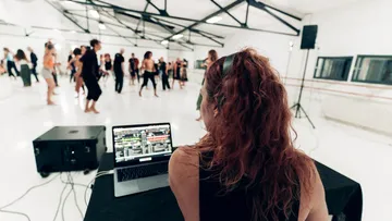 Tänzer bewegen sich in einem hellen Studio, während jemand Musik mischt.