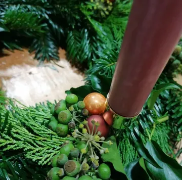 Kerze schmückt einen Adventskranz mit grünen Zweigen und Kugeln.