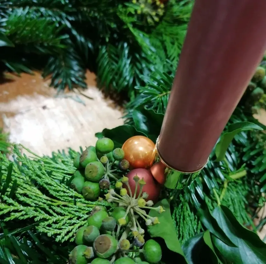 Candle adorns an Advent wreath with green branches and balls.