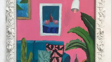 Colourful couch stands in front of pink wall with plants and pictures.