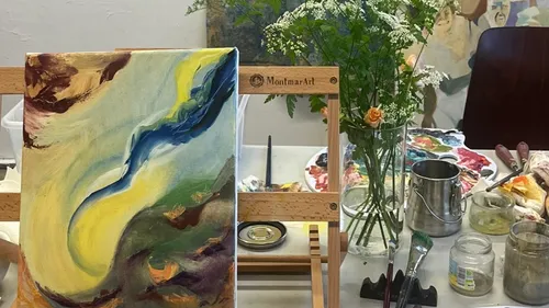 A canvas with abstract painting on a table surrounded by colors.