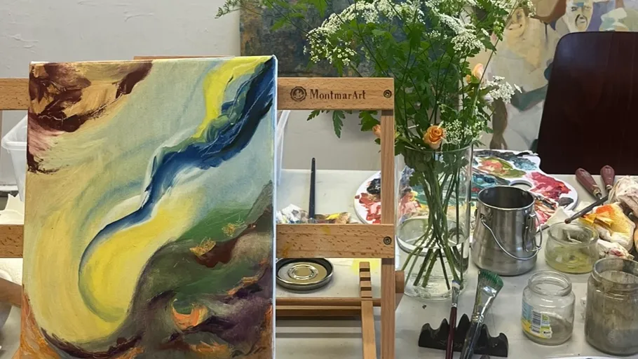 A canvas with abstract painting on a table surrounded by colors.