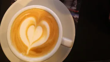 Coffee mug with heart pattern on foam, on a table.