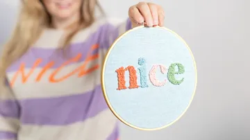 Embroidered frame with the word “nice” is held