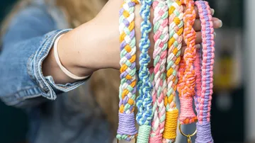 Bunte, geflochtene Armbänder werden von einer Hand gehalten.
