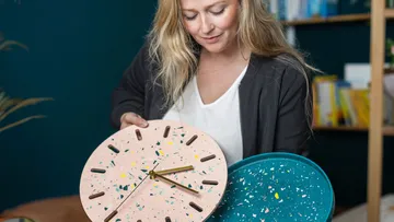 Woman holding two colorful clocks in a modern room.