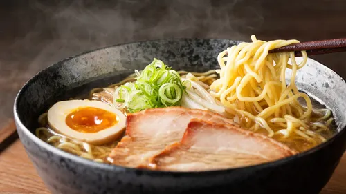 Nudeln werden mit Stäbchen aus einer Schüssel gehoben.