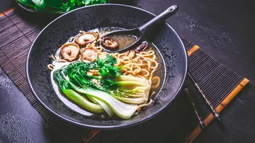 Schale mit Nudeln, Gemüse und Brühe auf Tischmatte.