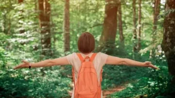 A person with a backpack stretches out arms in the forest.