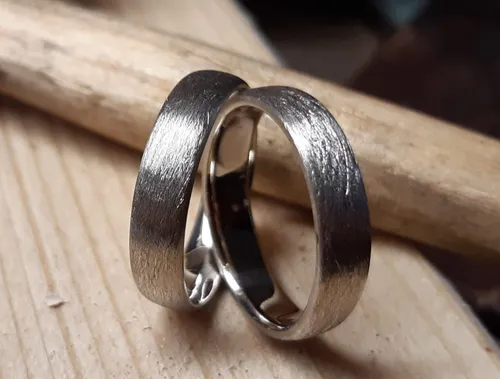 Wedding rings lie on wood, shiny and textured.