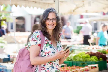 Woman smiles and looks at her cell phone at the market.