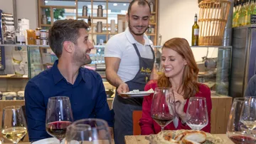 A waiter serves food to a smiling couple in the restaurant.