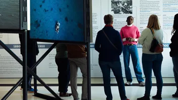 A presenter explains to a group of people in an exhibition room.