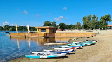 Stand-up paddle boards lie on the beach in front of a water building.