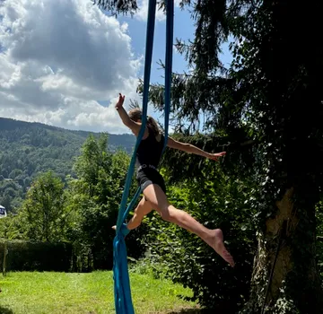 Mädchen schwingt an blauen Tüchern in einer grünen Umgebung.