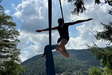 Eine Artistin schwingt an Tüchern vor einem Bergpanorama.