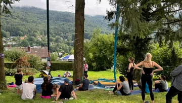 Menschen sitzen im Gras, während jemand an einem Pfahl hängt.