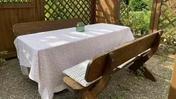 Holztisch mit Tischdecke und Stühlen in einem Garten.