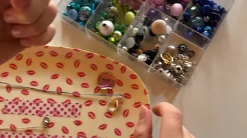 Eine Hand hält Schmuckstücke auf einem Lippen-musterierten Teller, daneben Perlen.