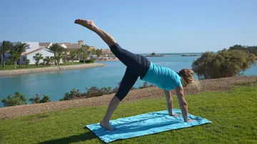 Woman doing yoga in the meadow by the water.